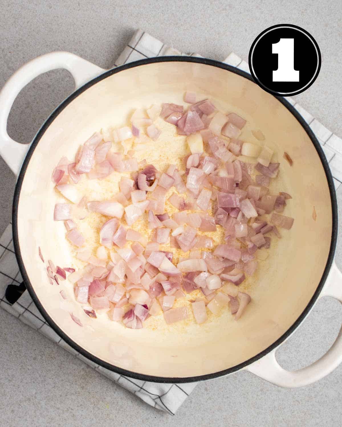 Cooked onion in a white Dutch oven on a folded white teacloth.