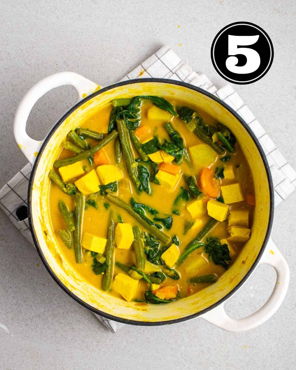 A pot of cooked vegetable yellow curry in a Dutch oven on a white folded teacloth.