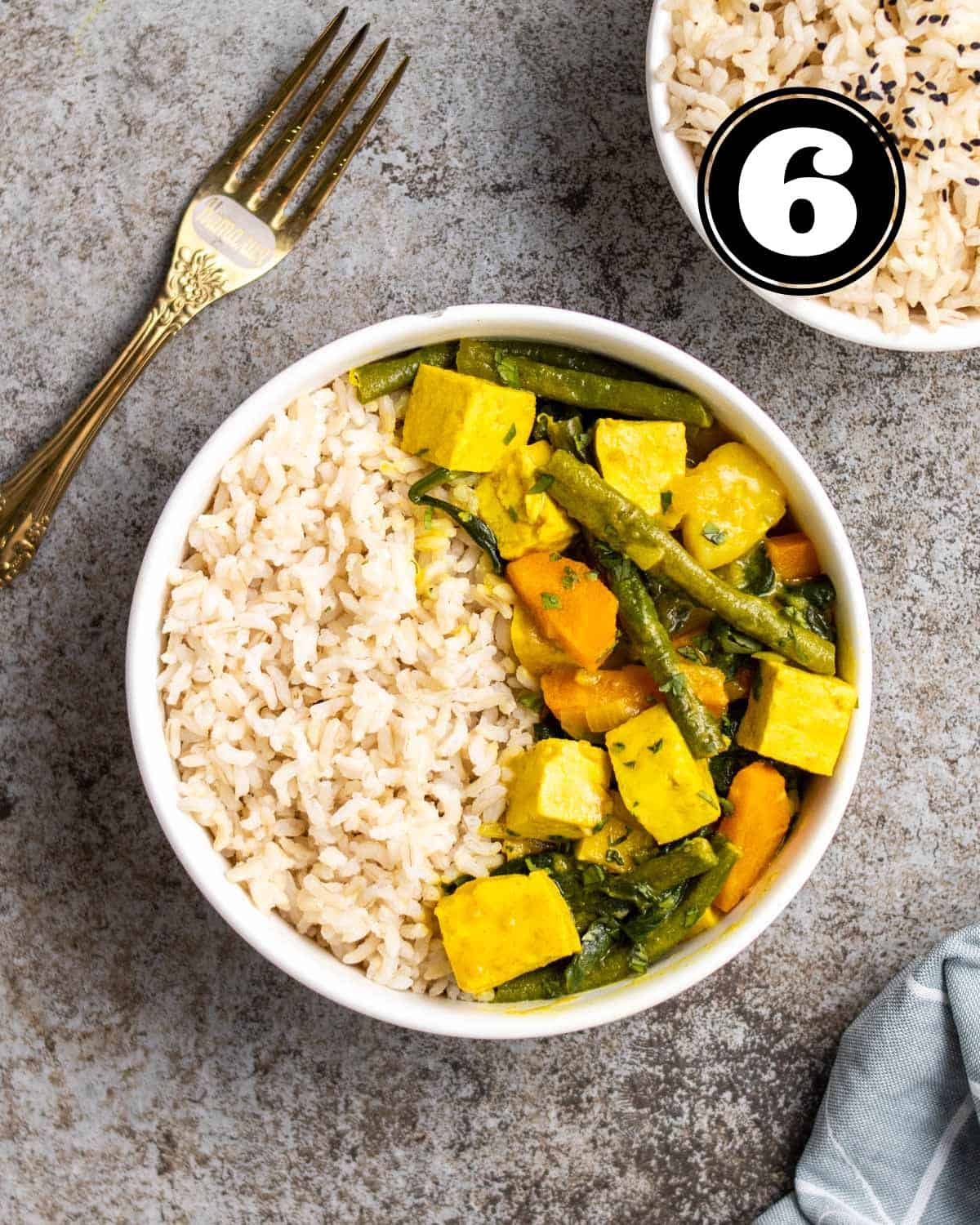 A bowl of yellow curry served with rice with a fork and bowl of rice beside.