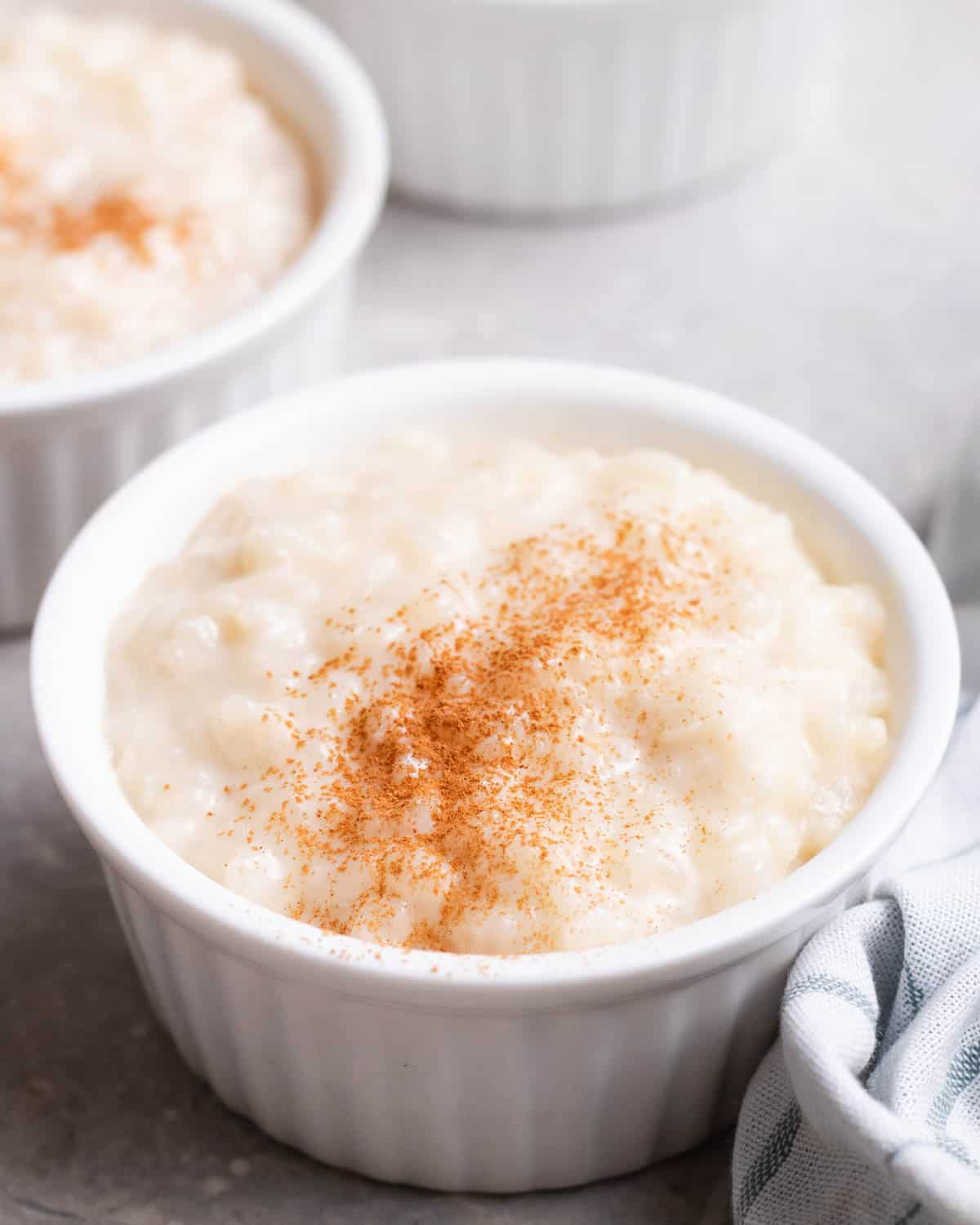 3 ramekins of rice pudding topped with cinnamon with a blue teacloth beside.
