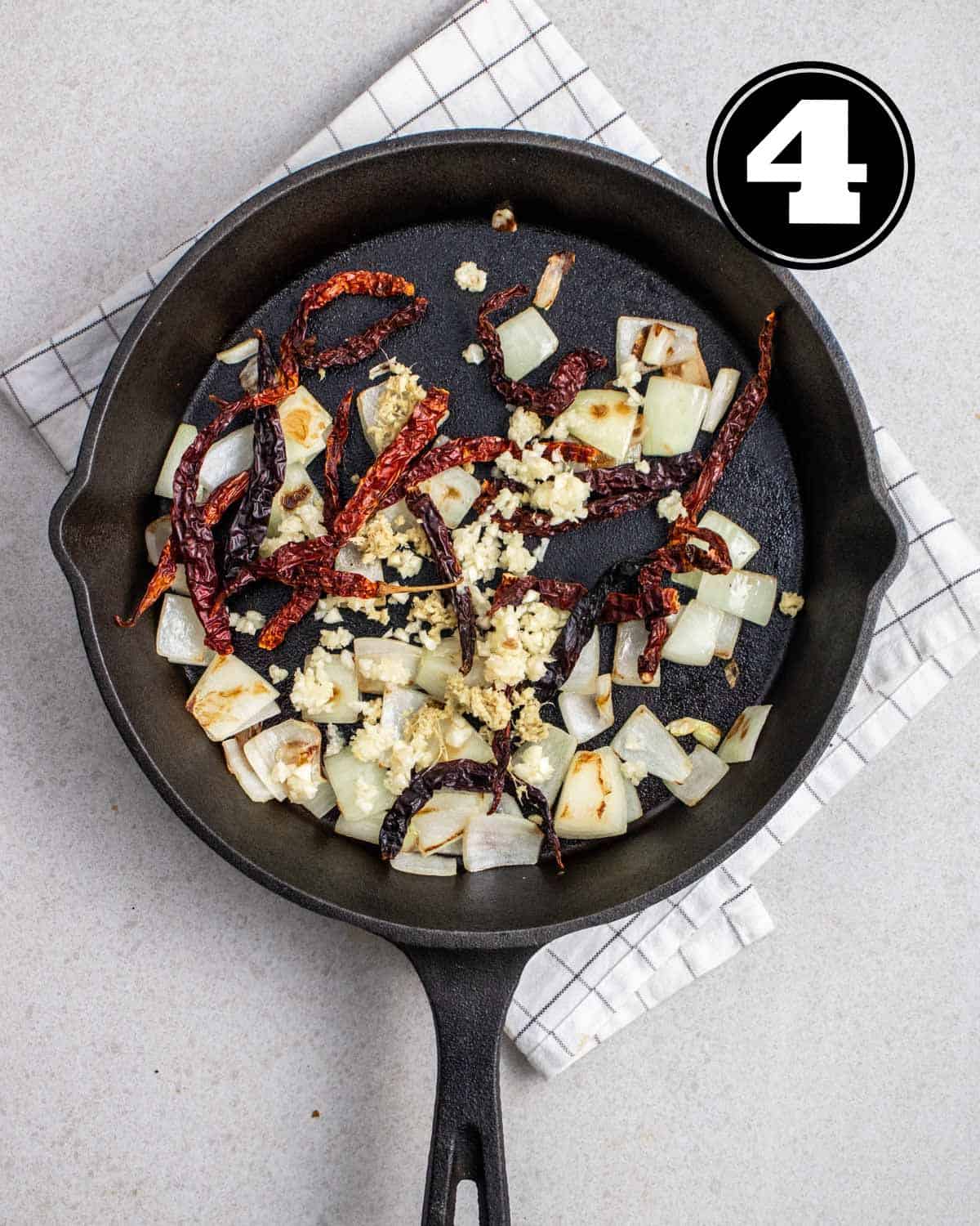 Cooked onion, garlic, dried chilies, and peppercorn in a cast iron pan.