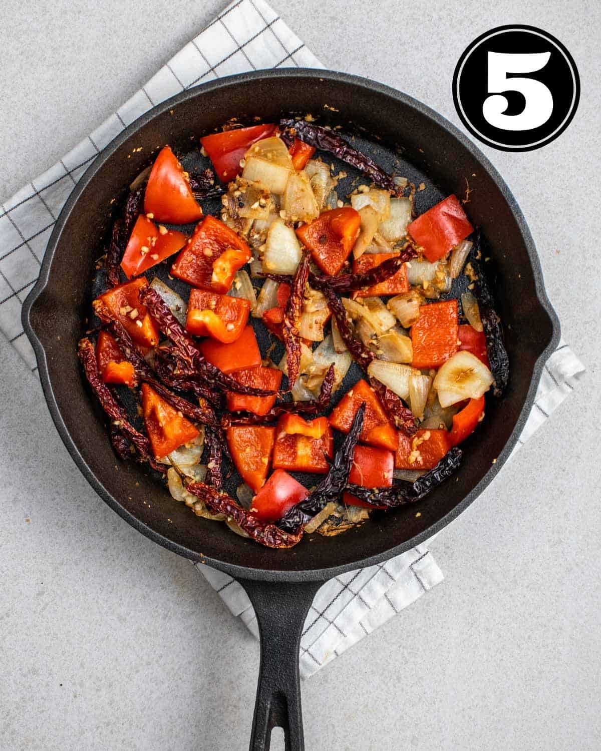 Adding red pepper to a pan of cooked aromatics in a cast iron pan.