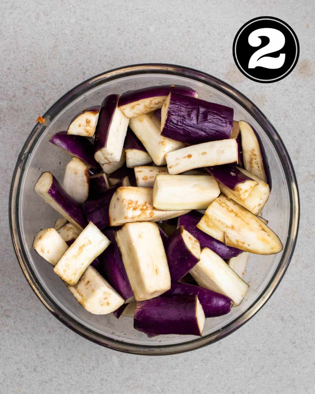 Slices of eggplant coated in salt in a glass bowl.