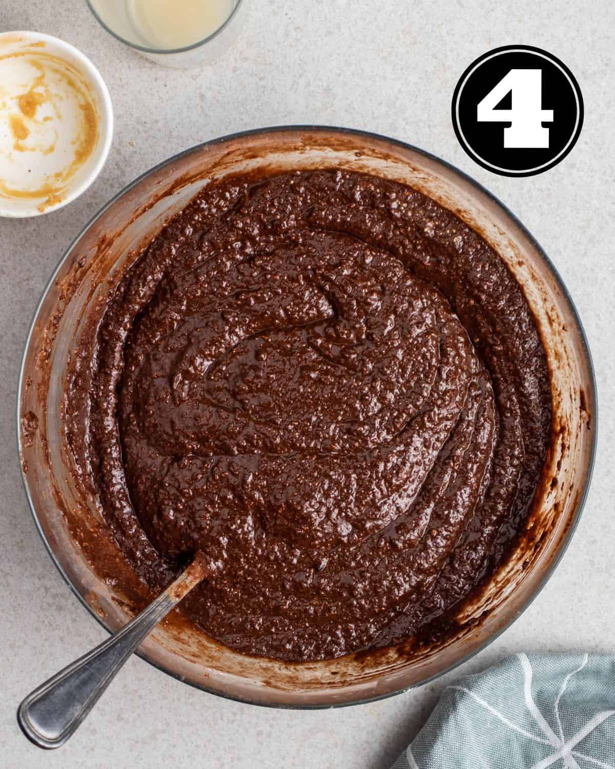Brownie batter in a glass bowl with a spoon beside.