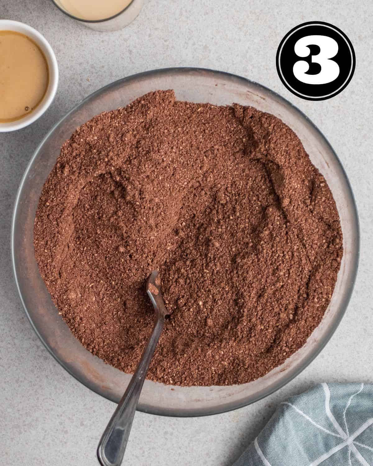 Dry ingredients in a glass bowl with a spoon beside.