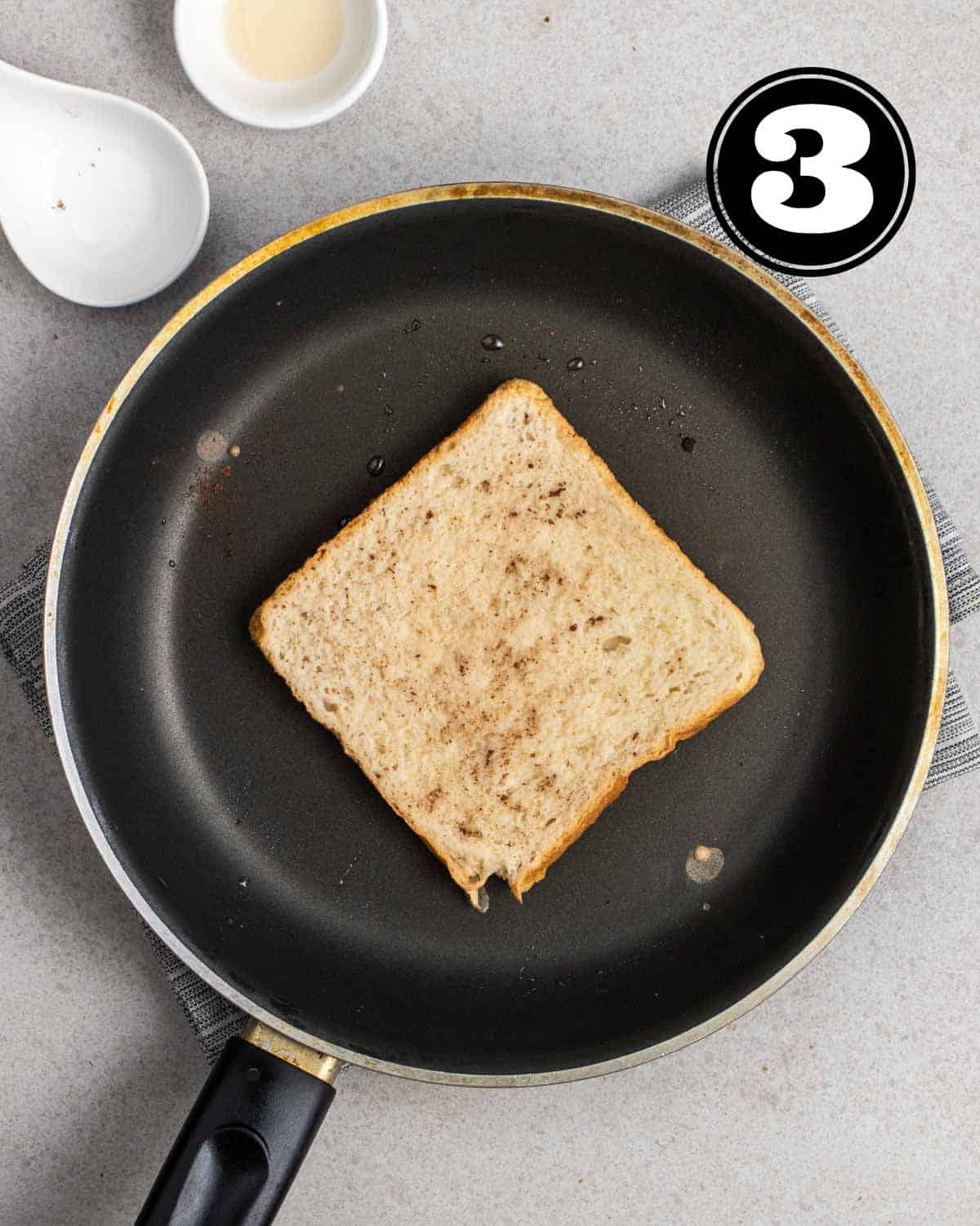 Cooking a piece of French toast in a non-stick pan with 2 empty sauce dishes beside.