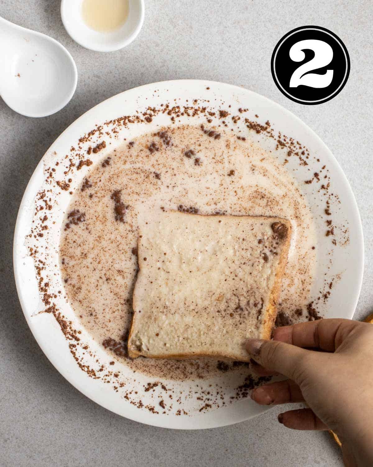 Dipping a slice of bread into a bowl of custard mixture with 2 empty sauce dishes beside.