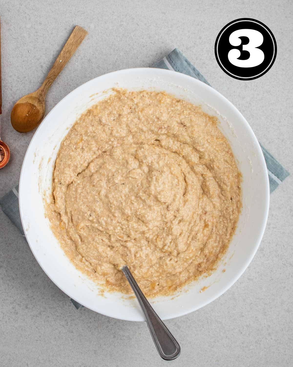 Banana bread batter in a bowl with a fork and wooden spoon beside.