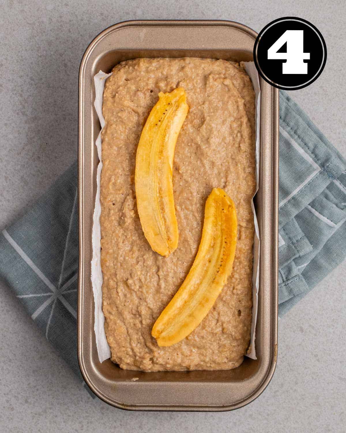 Banana bread batter in a loaf pan lined with parchment paper topped with banana halves.