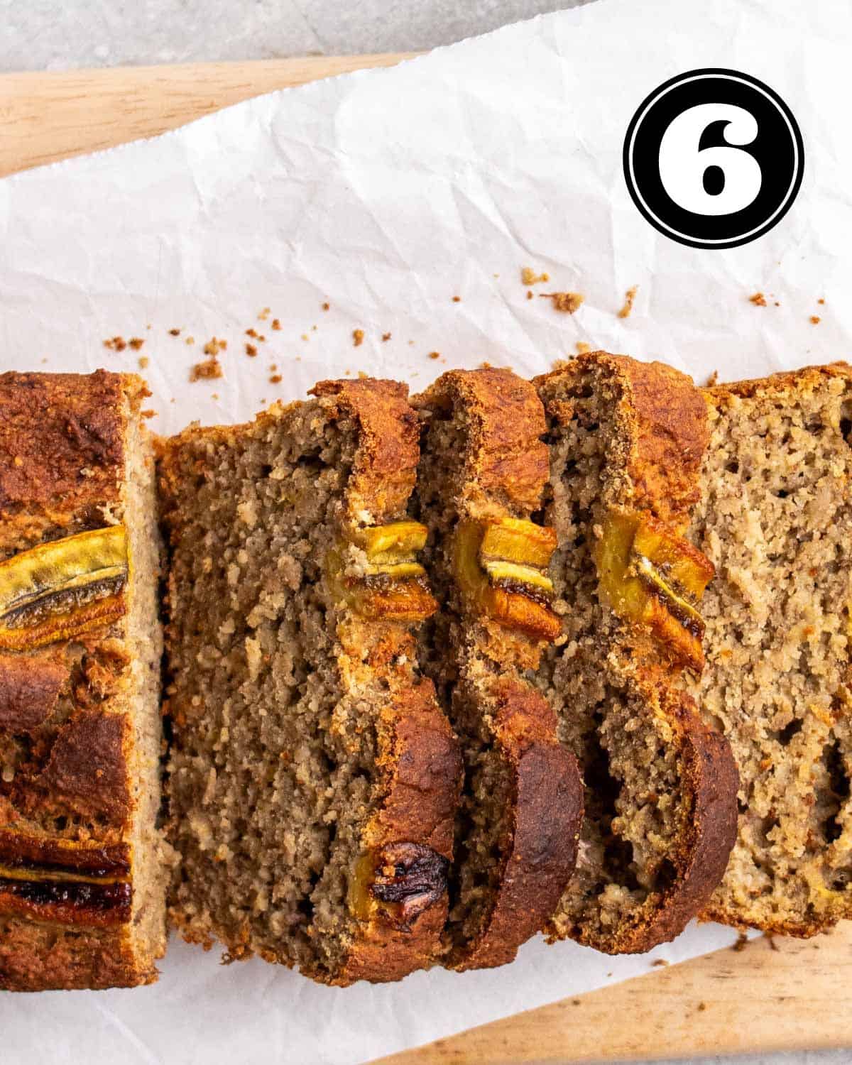 Partially sliced banana bread on a wooden board lined with parchment paper.