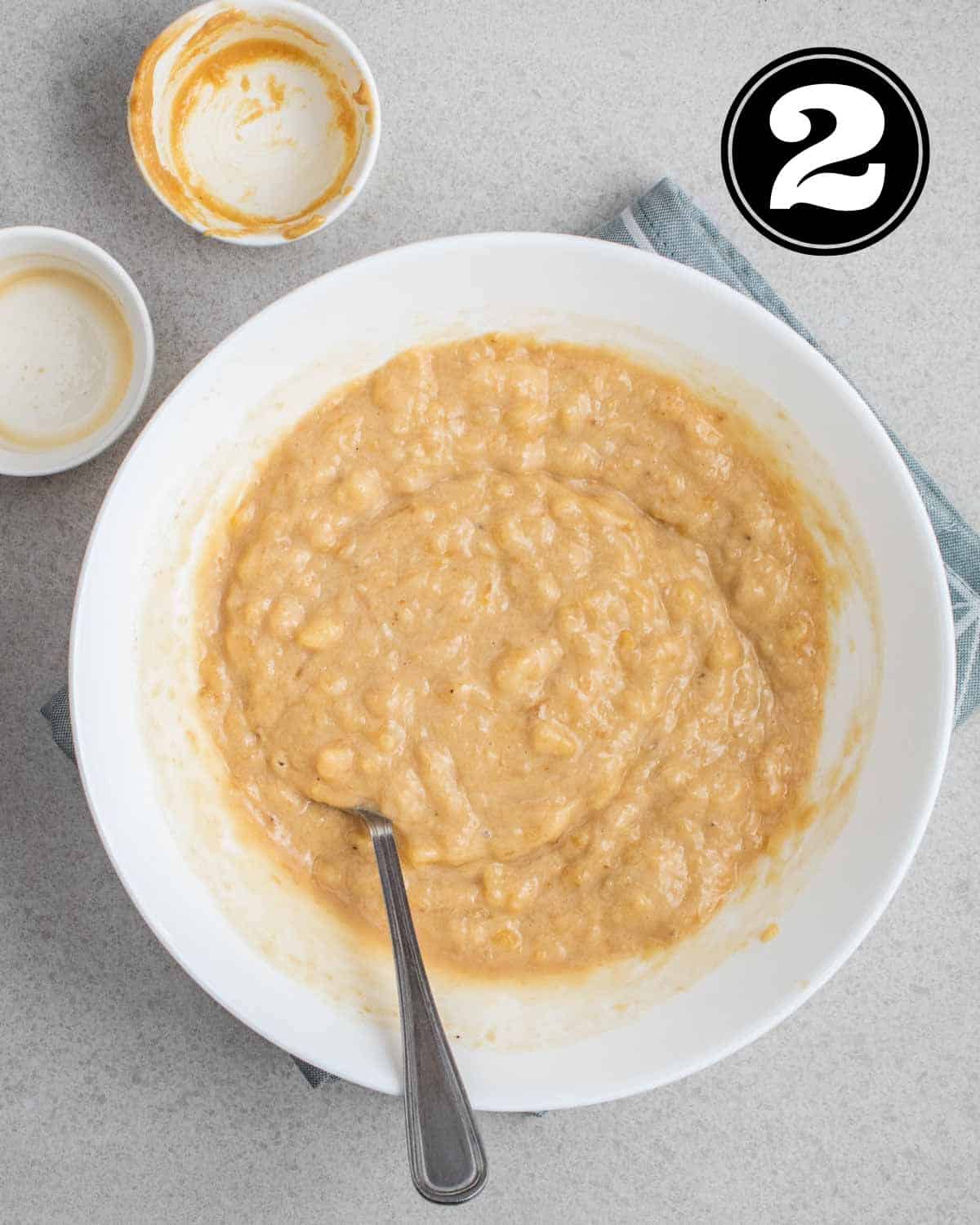 Wet ingredients in a bowl with a fork and 2 empty ramekins beside.