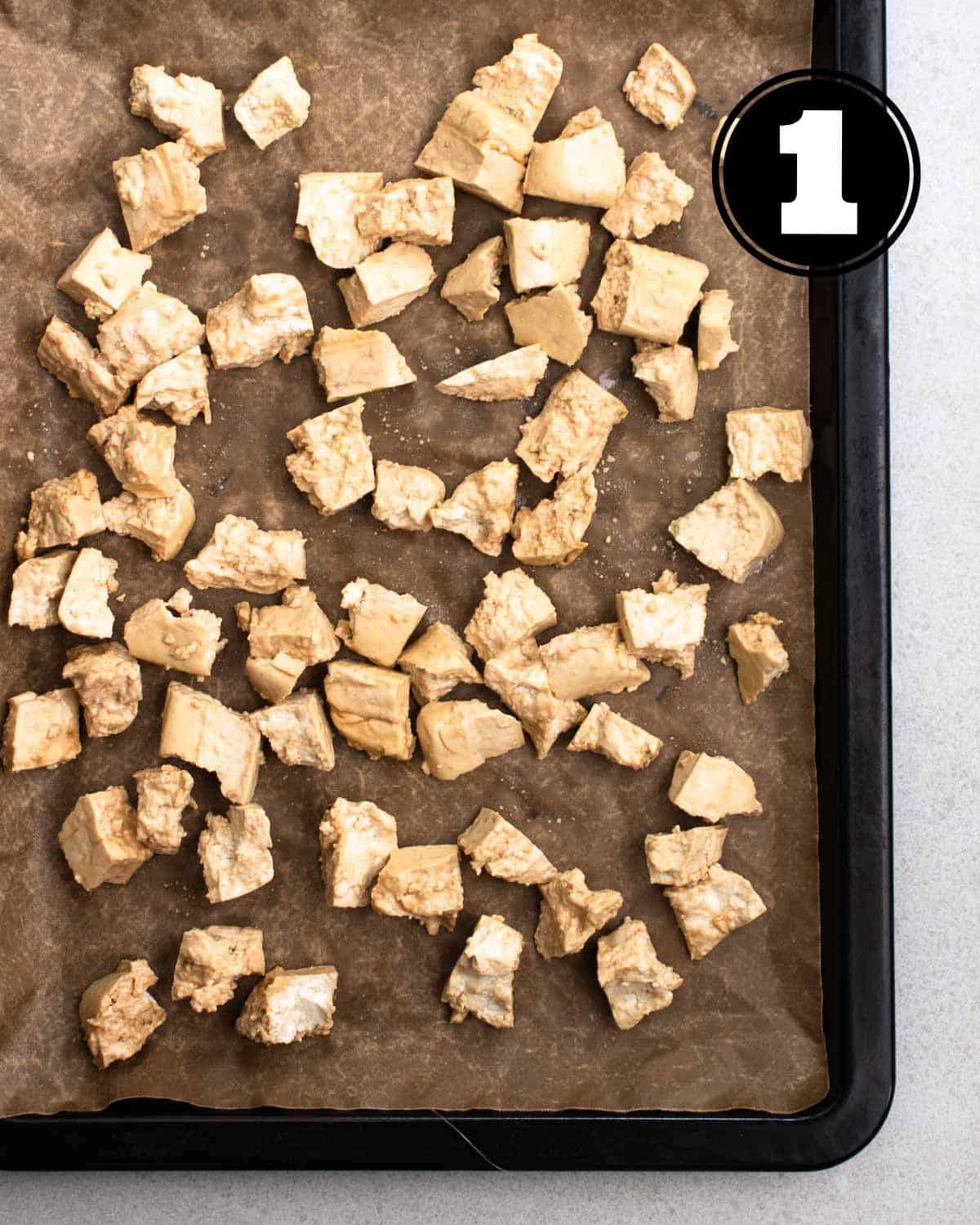 Tofu pieces coated in cornstarch on a baking tray lined with parchment paper.