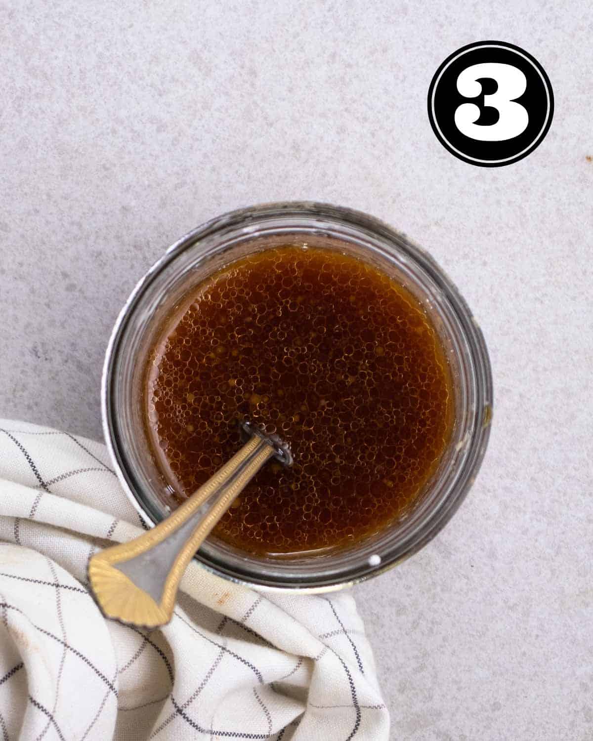 A glass jar containing all seasonings needed for teriyaki sauce with a spoon beside.