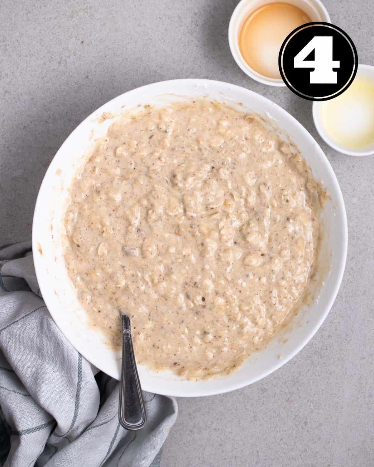 Muffin batter in a mixing bowl with a fork with 2 empty ramekins beside.