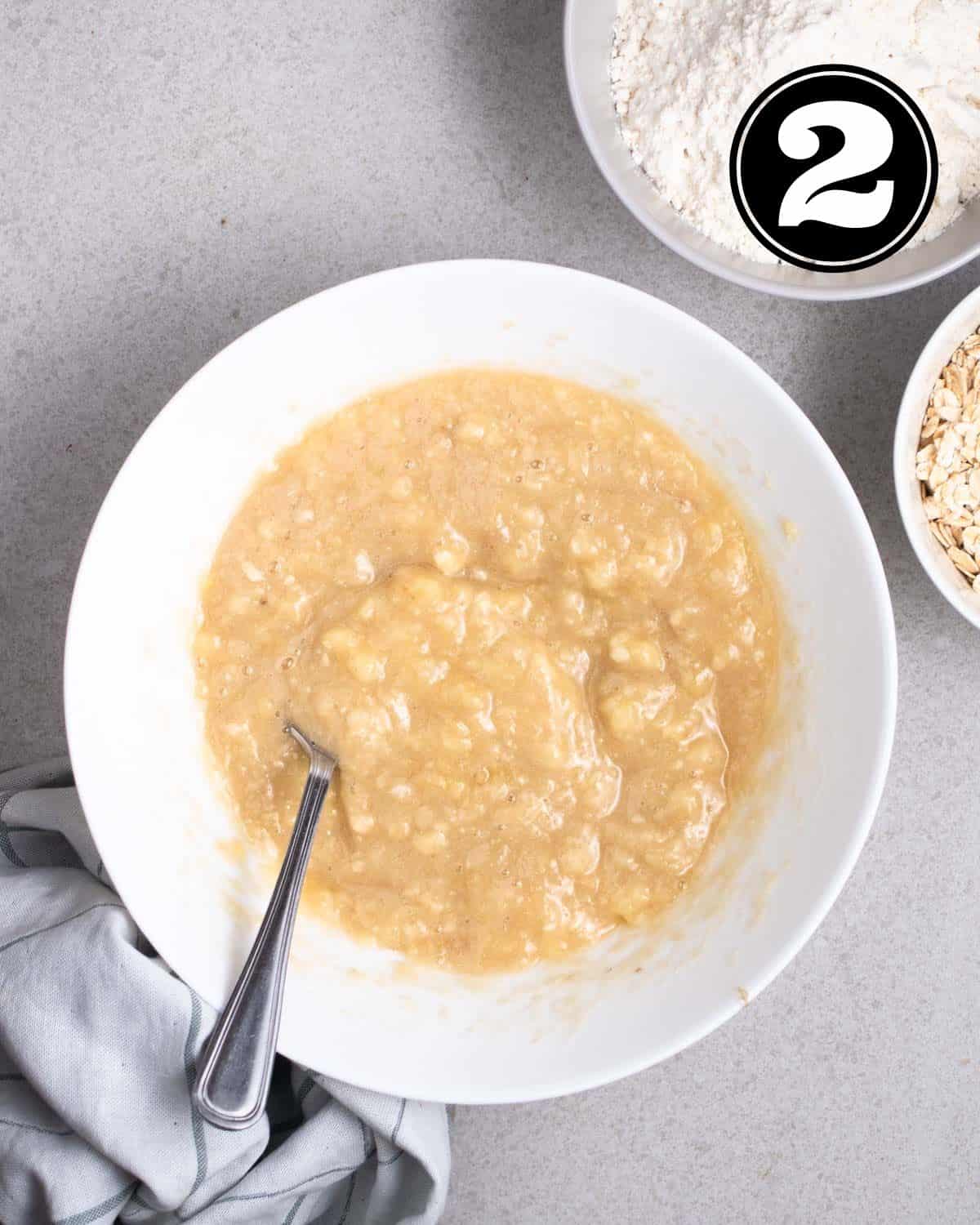 Mashed bananas in a white mixing bowl with a fork beside.