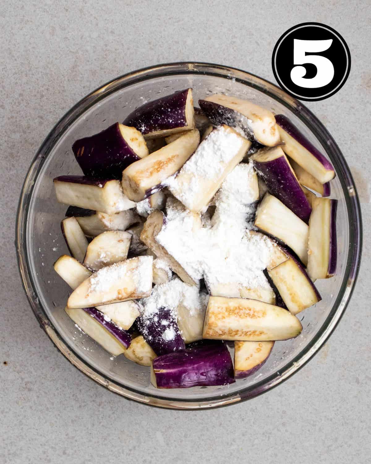 Adding cornstarch to a bowl of eggplant slices.