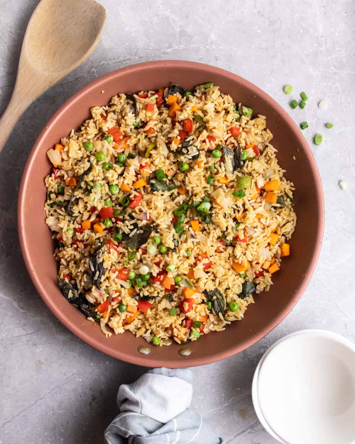 A pan of fried rice with a wooden spatula and bowls beside.