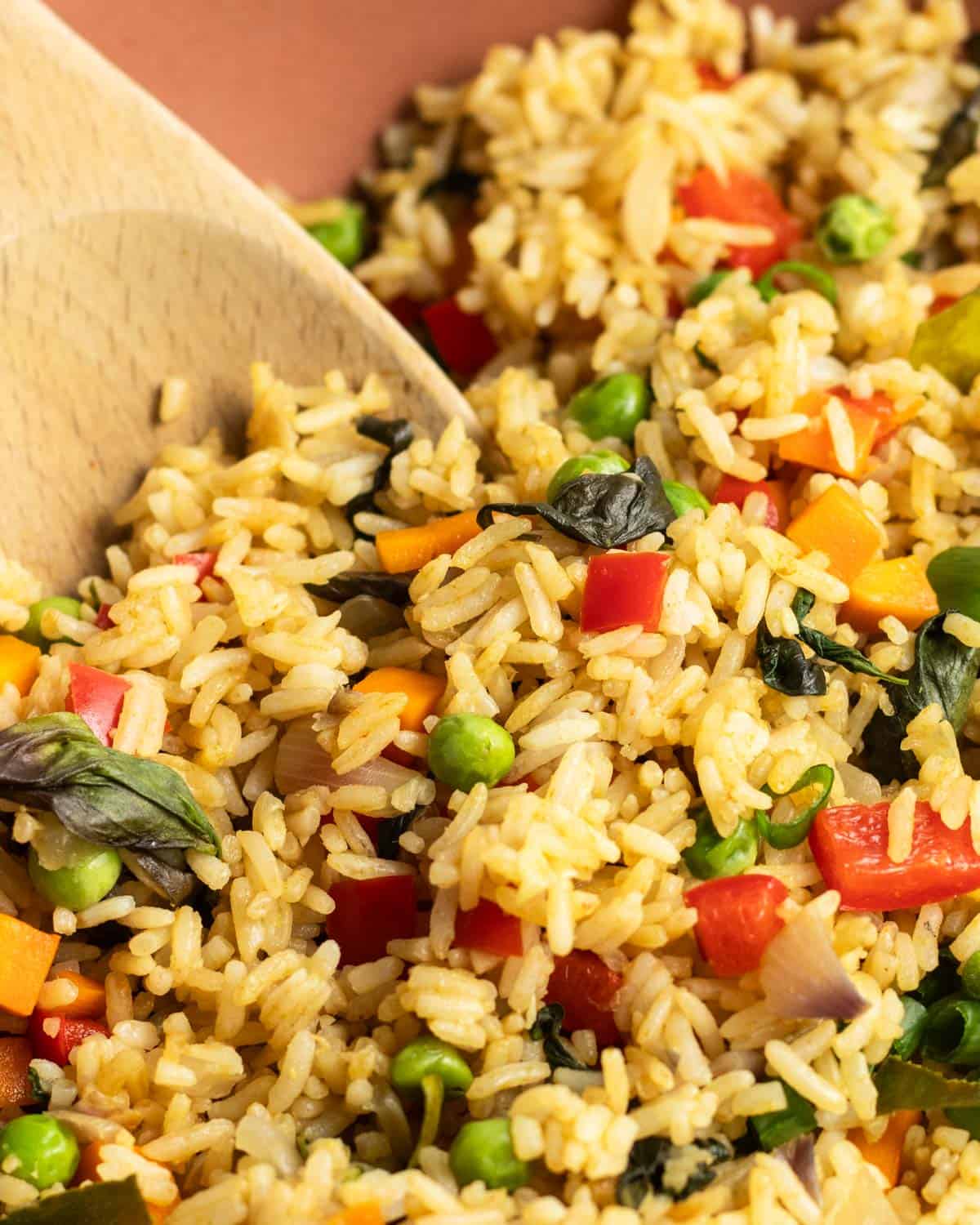 A pan of curry fried rice with a wooden spatula beside.