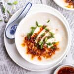 a bowl of congee served on a plate with a ceramic spoon beside.