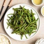 A plate of green beans served with chopsticks with a bowl of rice and 2 cups of tea beside.