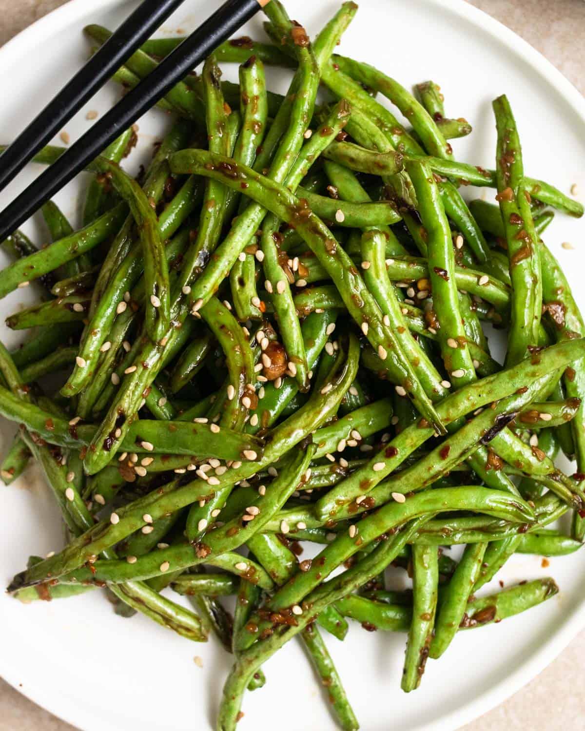 A plate of green beans topped with sesame seeds and served with chopsticks.