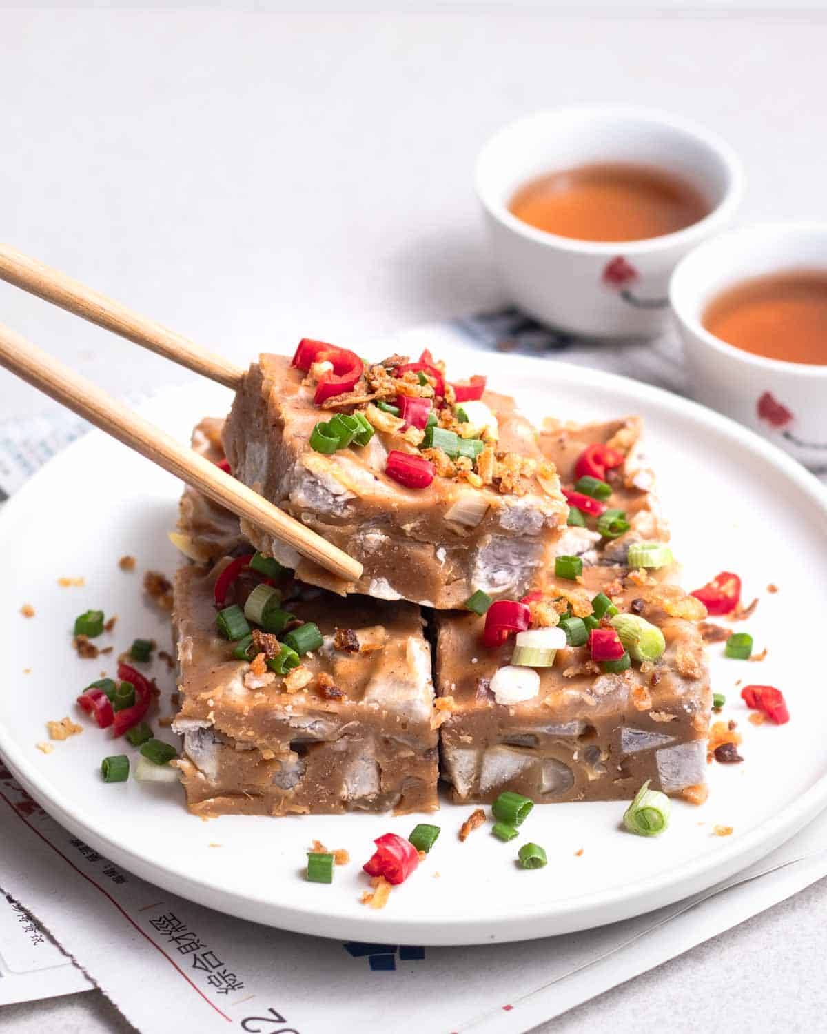 Taking out a piece of taro cake from a plate with a pair of chopsticks.