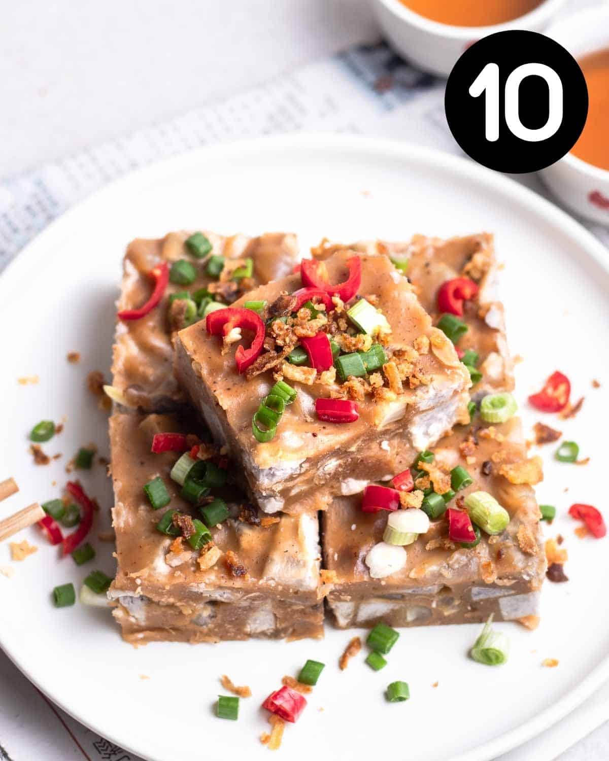 Slices of yam cake on a plate topped with chiles, green onion, and fried shallots.