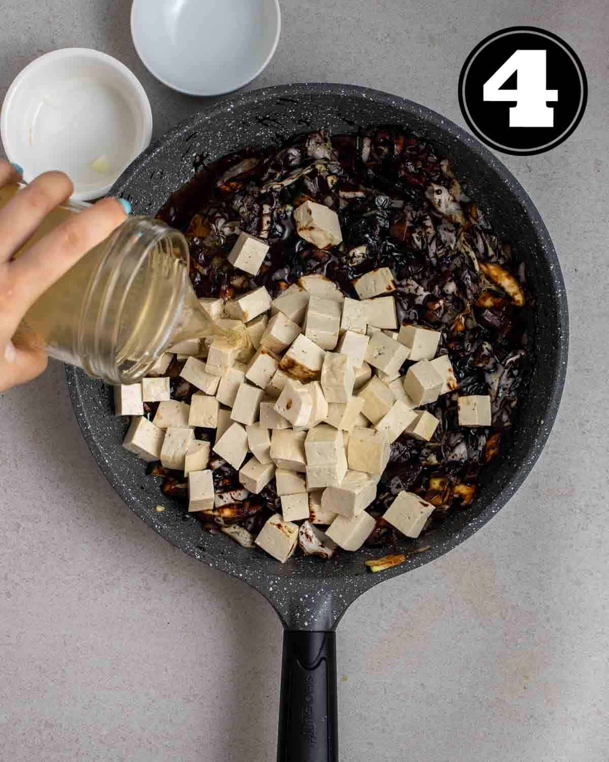 Adding broth and tofu into a pan of cooked veggies.