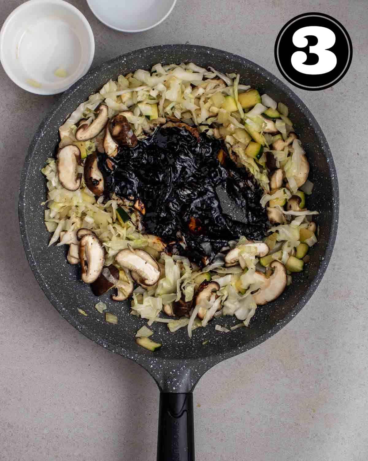 Frying chunjang in the middle of a pan of cooked veggies with 2 empty ramekin beside.