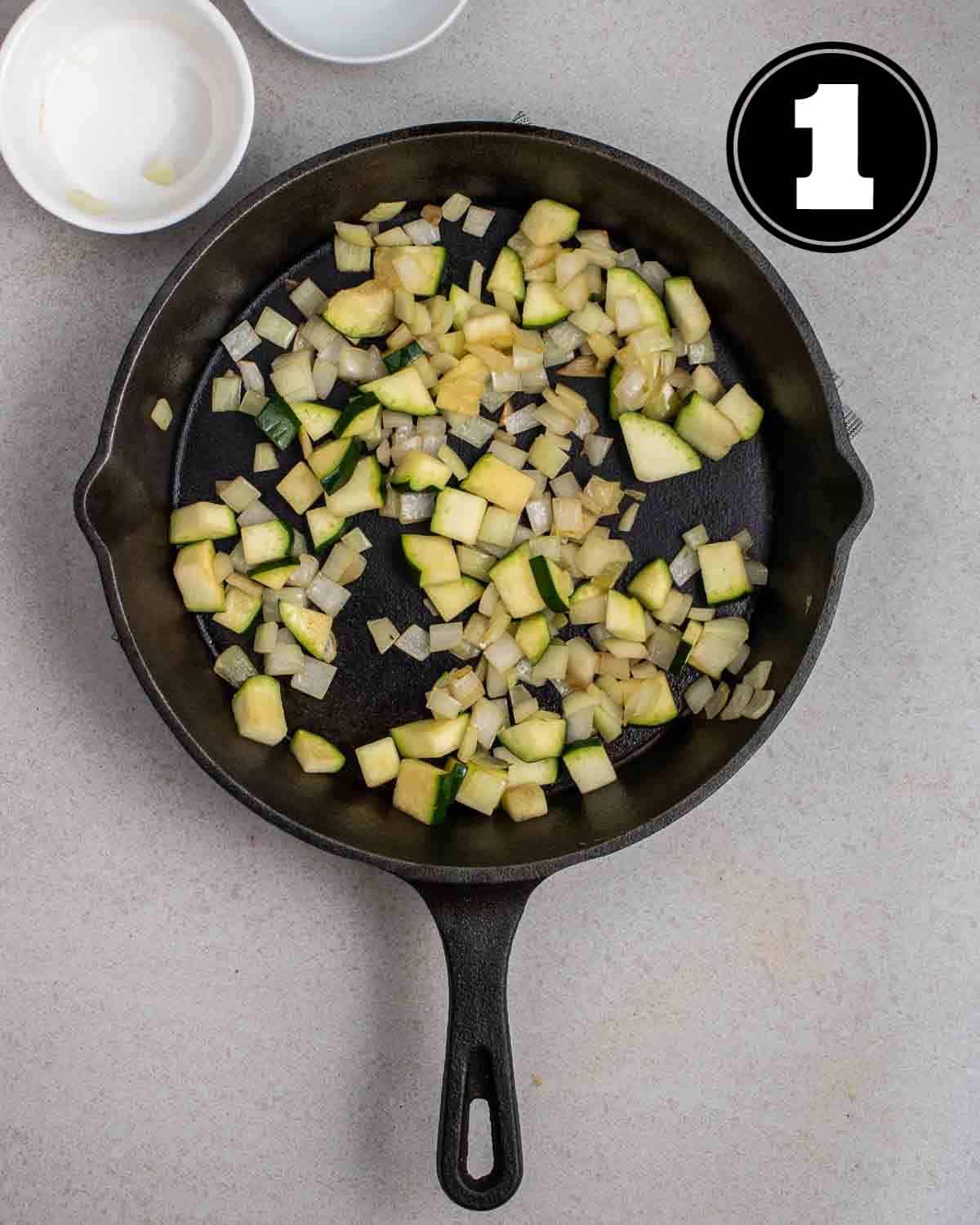 Cooked onion and zucchini in a pan with 2 ramekins beside.