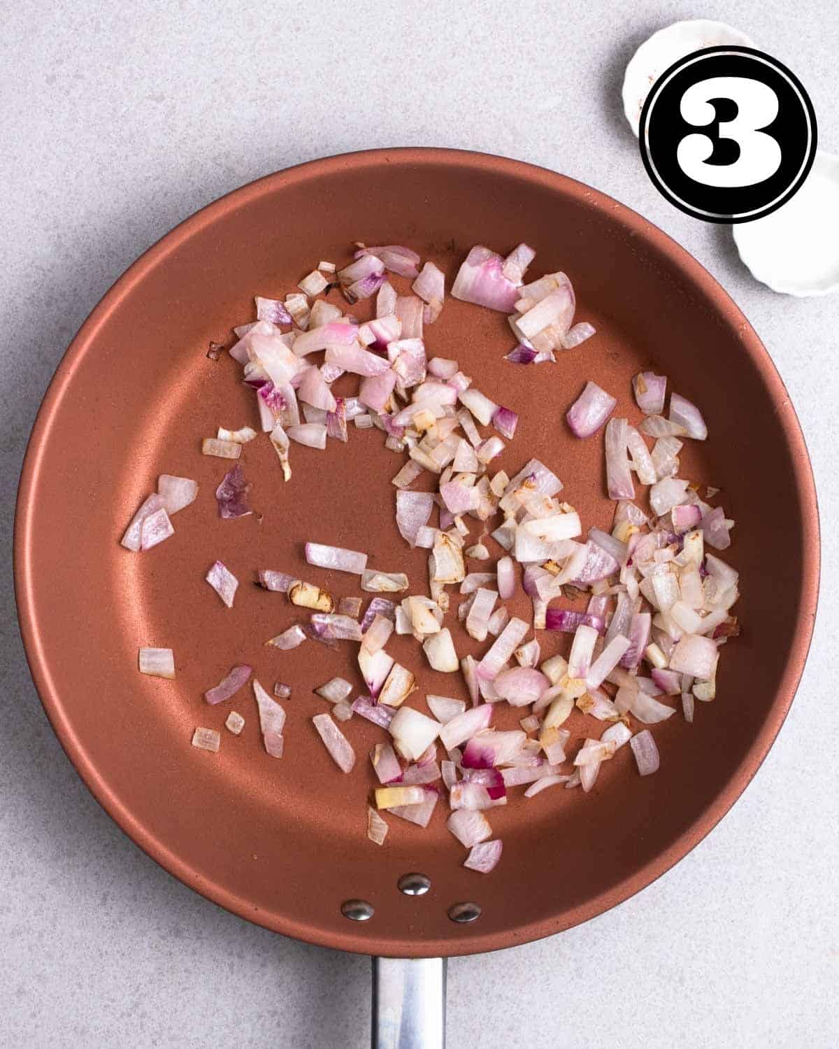 Cooked shallots in a pan with 2 empty sauce dishes beside.