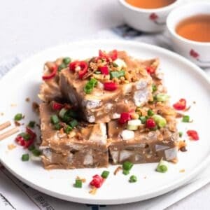 A plate of yam cake slices with pair of chopsticks and 2 cups of tea in the background.