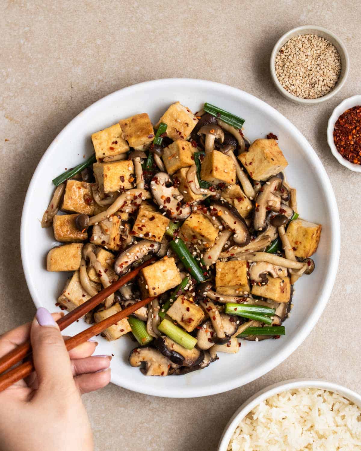 Stirring a plate of mushroom tofu stir-fry with a pair of chopsticks.