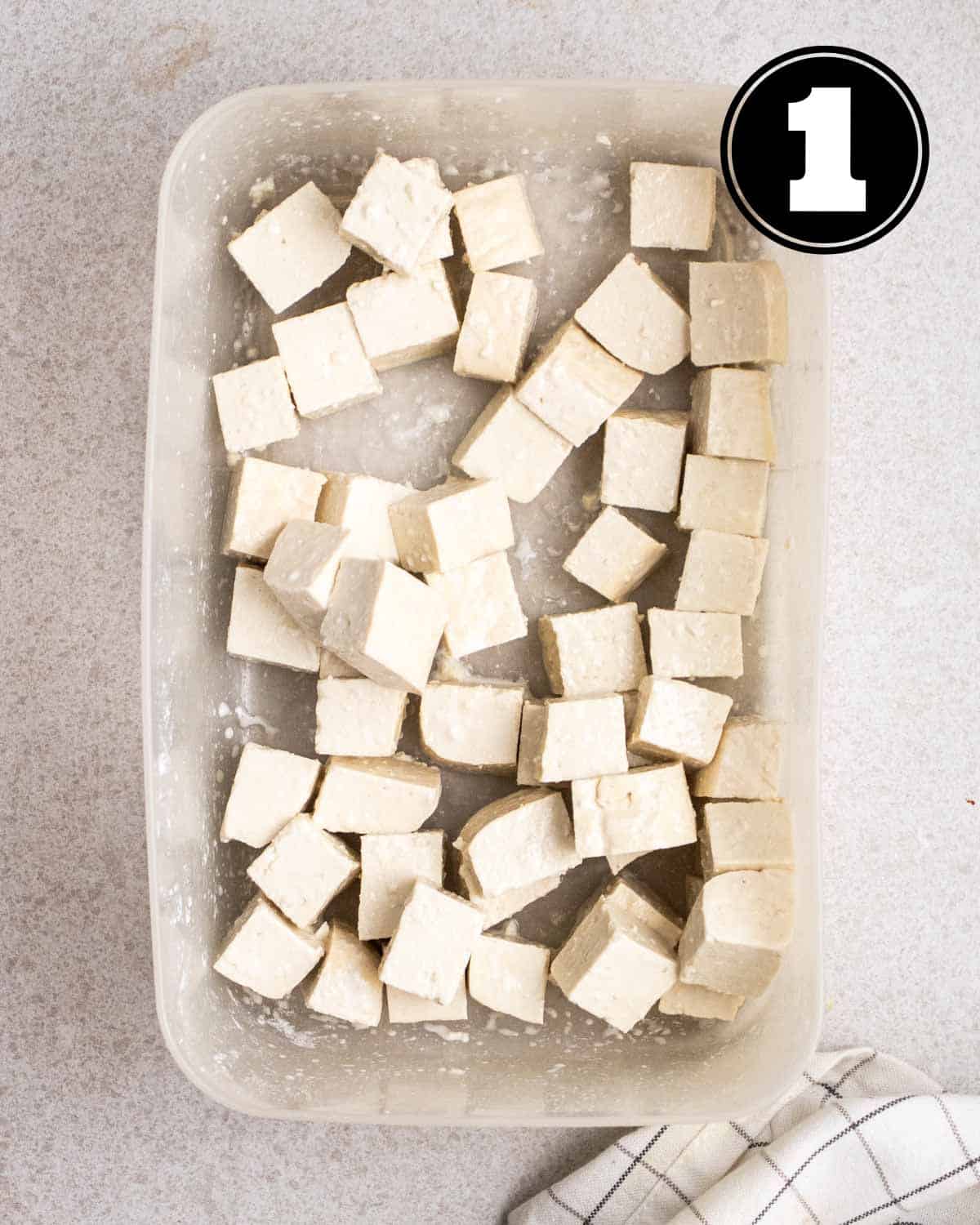 Tofu coated in cornstarch in a rectangular container.