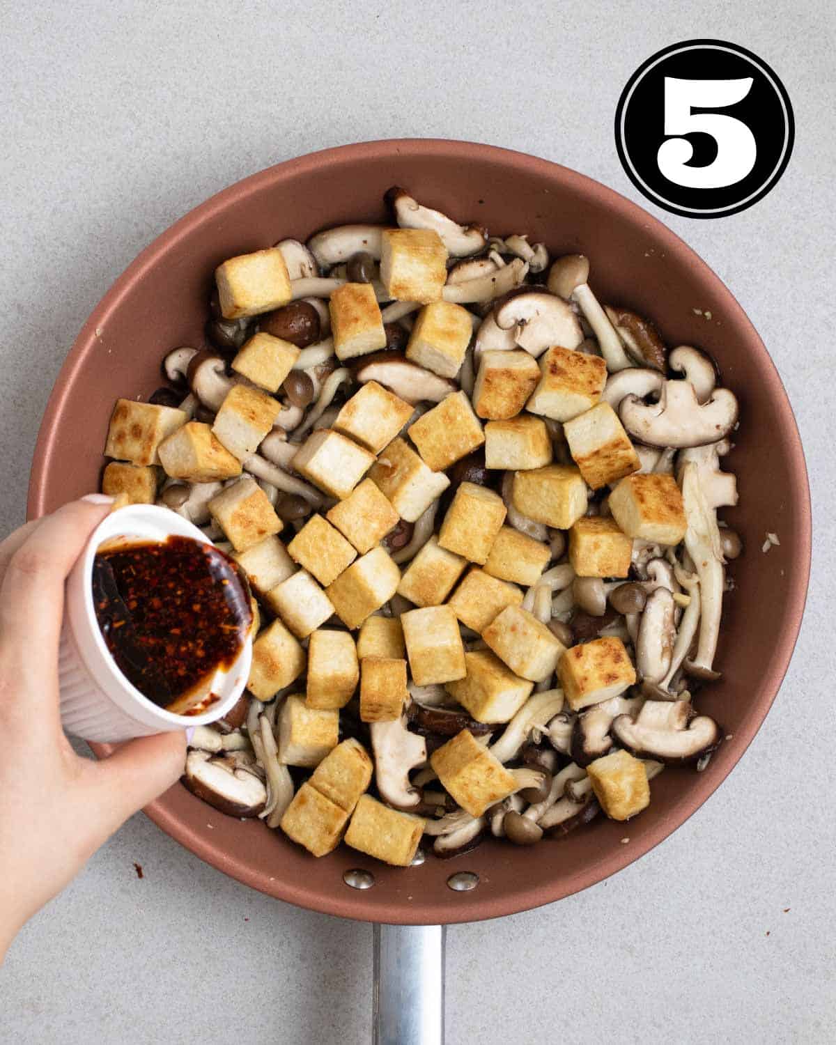 Pouring stir-fry sauce into a pan of tofu and mushrooms.
