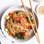 A plate of japchae served with chopsticks with sesame seeds and soy sauce.