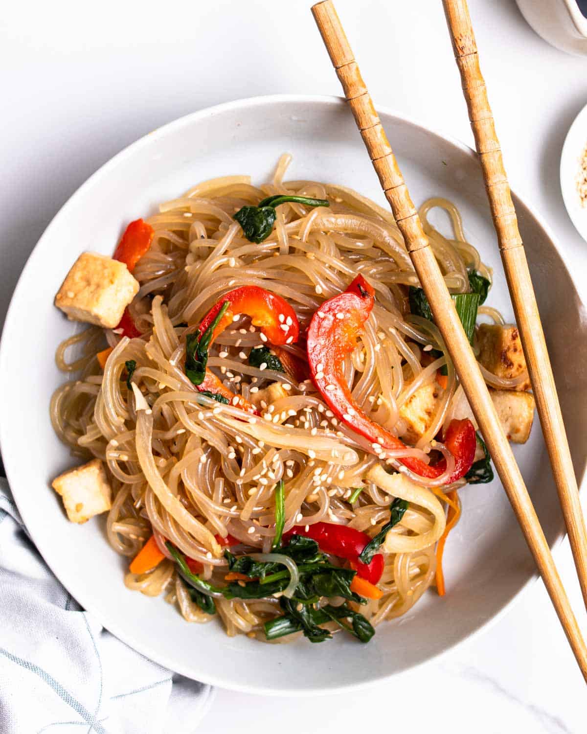 A plate of japchae served with chopsticks with a blue teacloth beside.