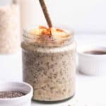 A jar of overnight oats served with spoon with oats, milk, and maple syrup in the background.