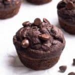 Chocolate muffins arranged on a parchment paper with chocolate chips beside.