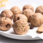 A plate of protein balls with a spoonful of peanut butter beside and a cup of coffee in the background.