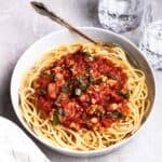A bowl of spaghetti served with sauce with 2 glasses of water in a background.