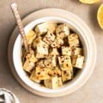 A bowl of tofu feta served with a teaspoon on a brown plate.