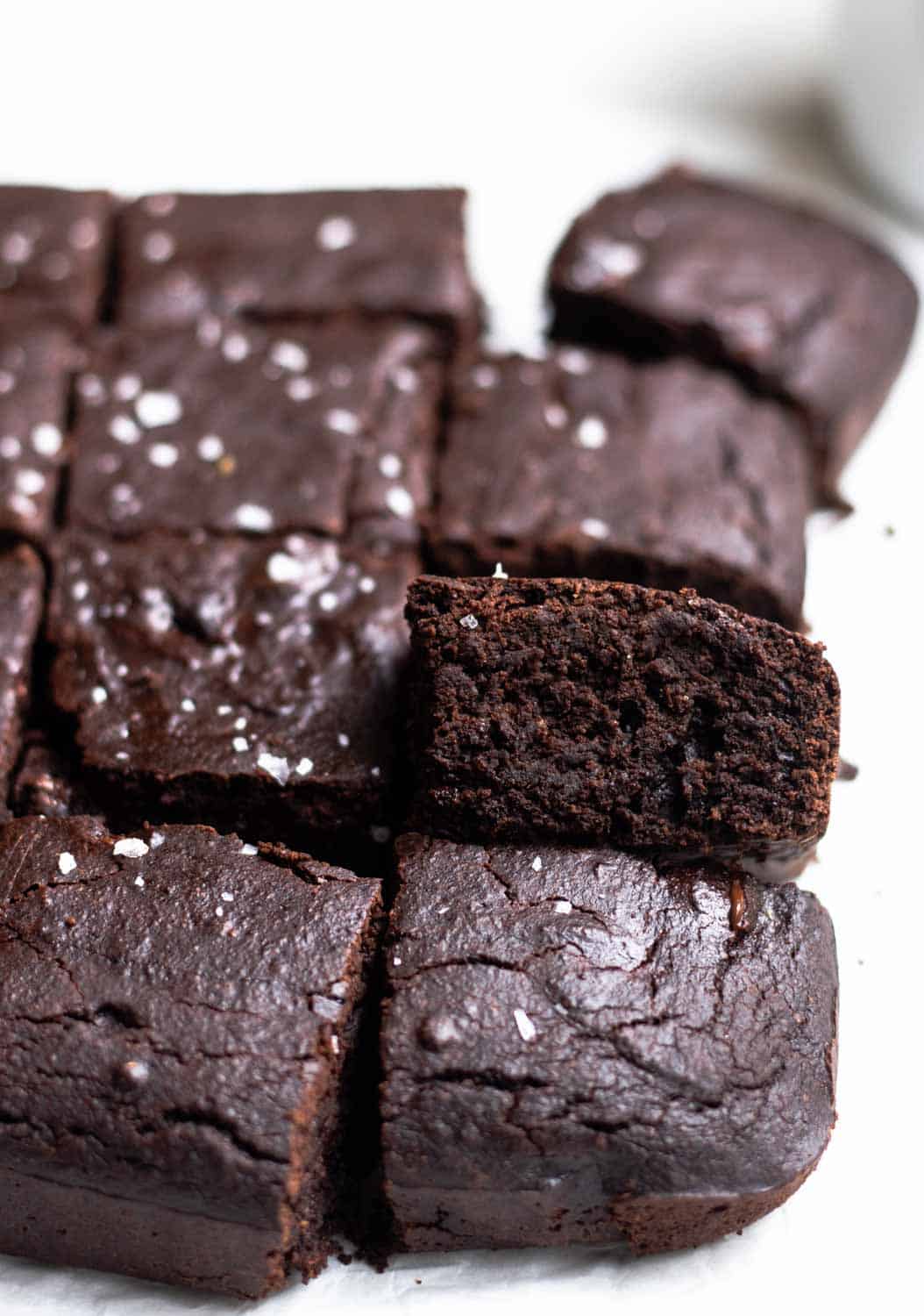A tray of brownies arranged on a parchment paper topped with flaked sea salt.