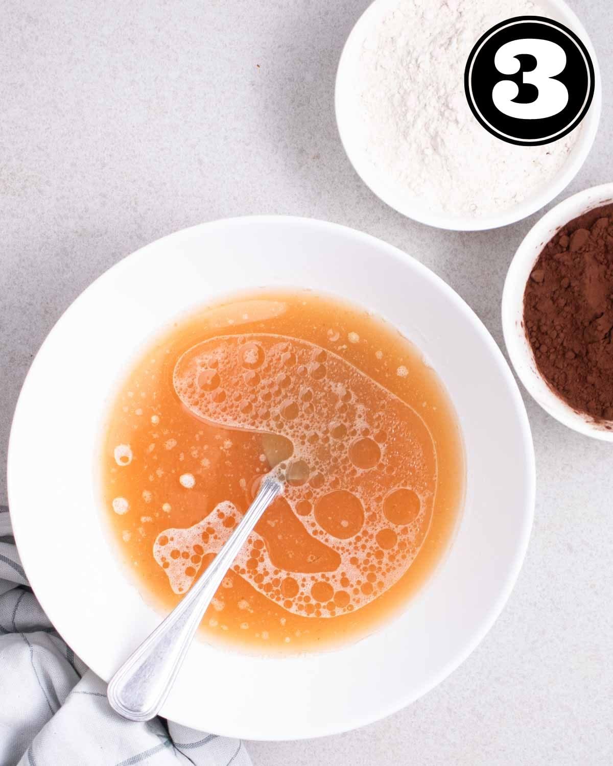 Wet ingredients in a bowl with a fork beside and a bowl of oat flour and cocoa powder in the background.