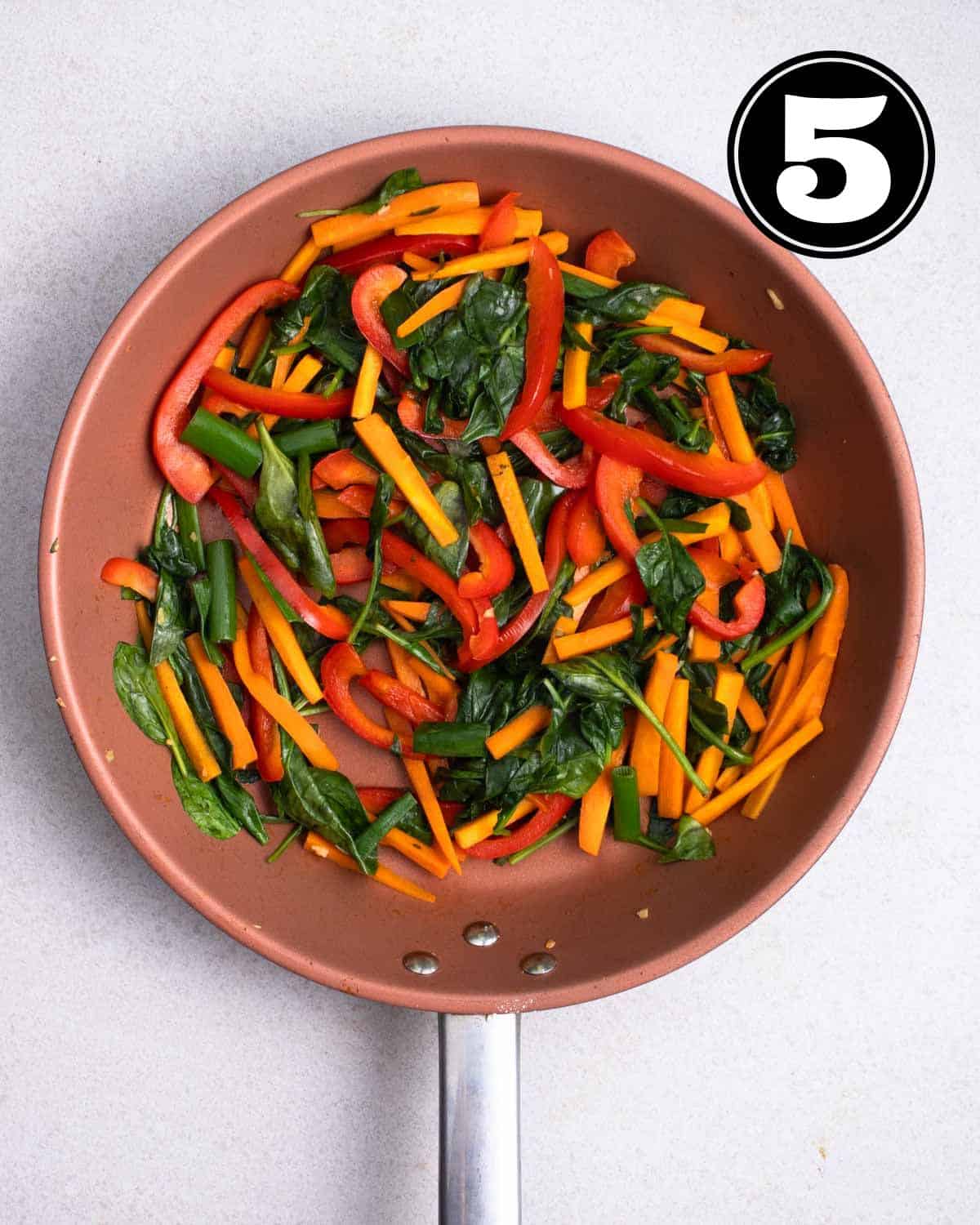Cooked carrot, bell pepper, and spinach in a non-stick pan.