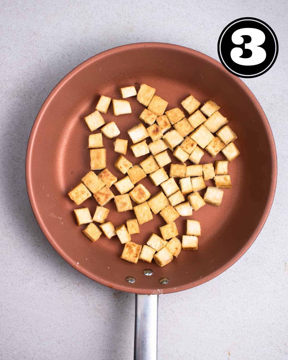 Pan-fried tofu cubes in a non-stick pan.