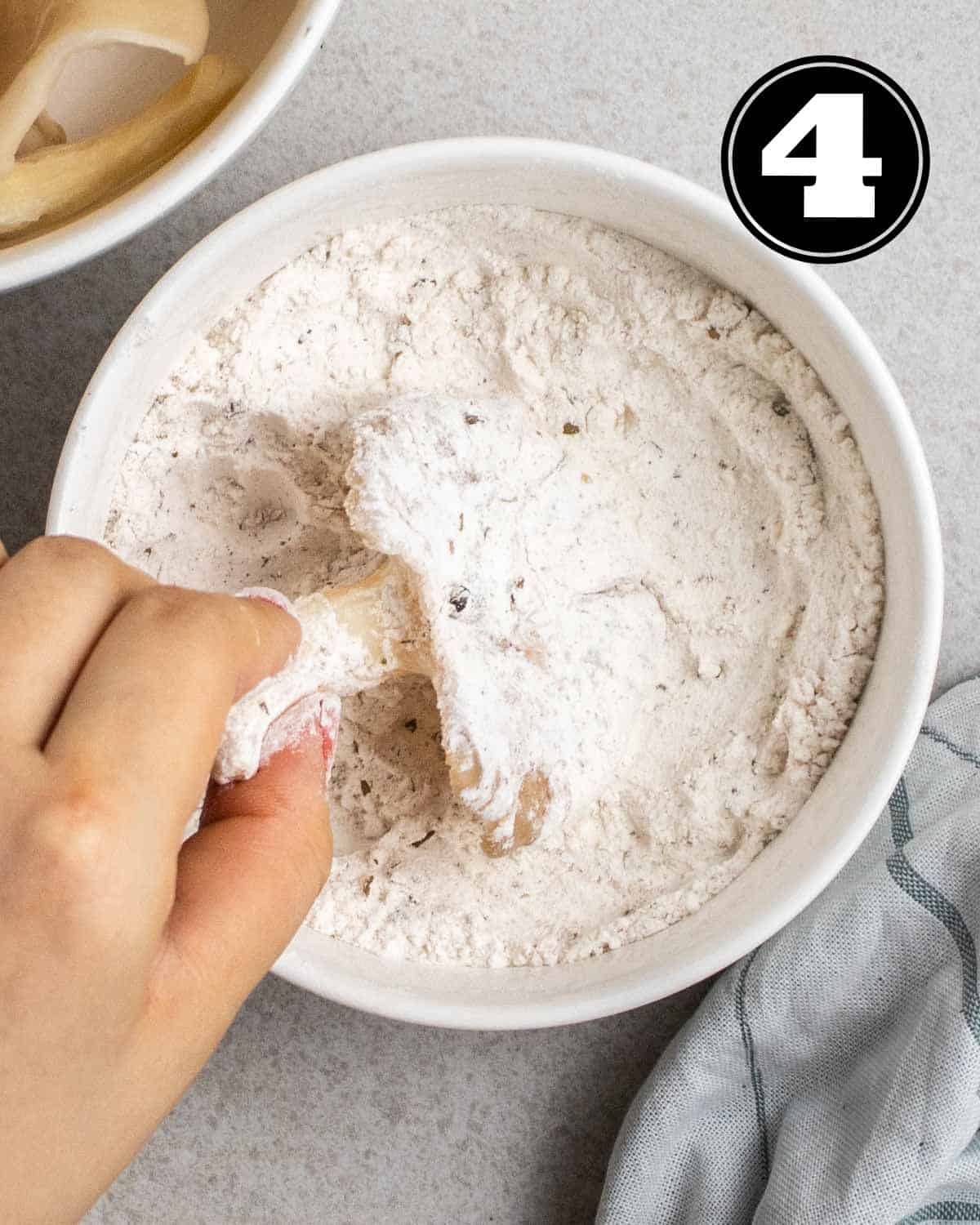 Dipping oyster mushrooms in flour with a bowl of oyster mushrooms beside.