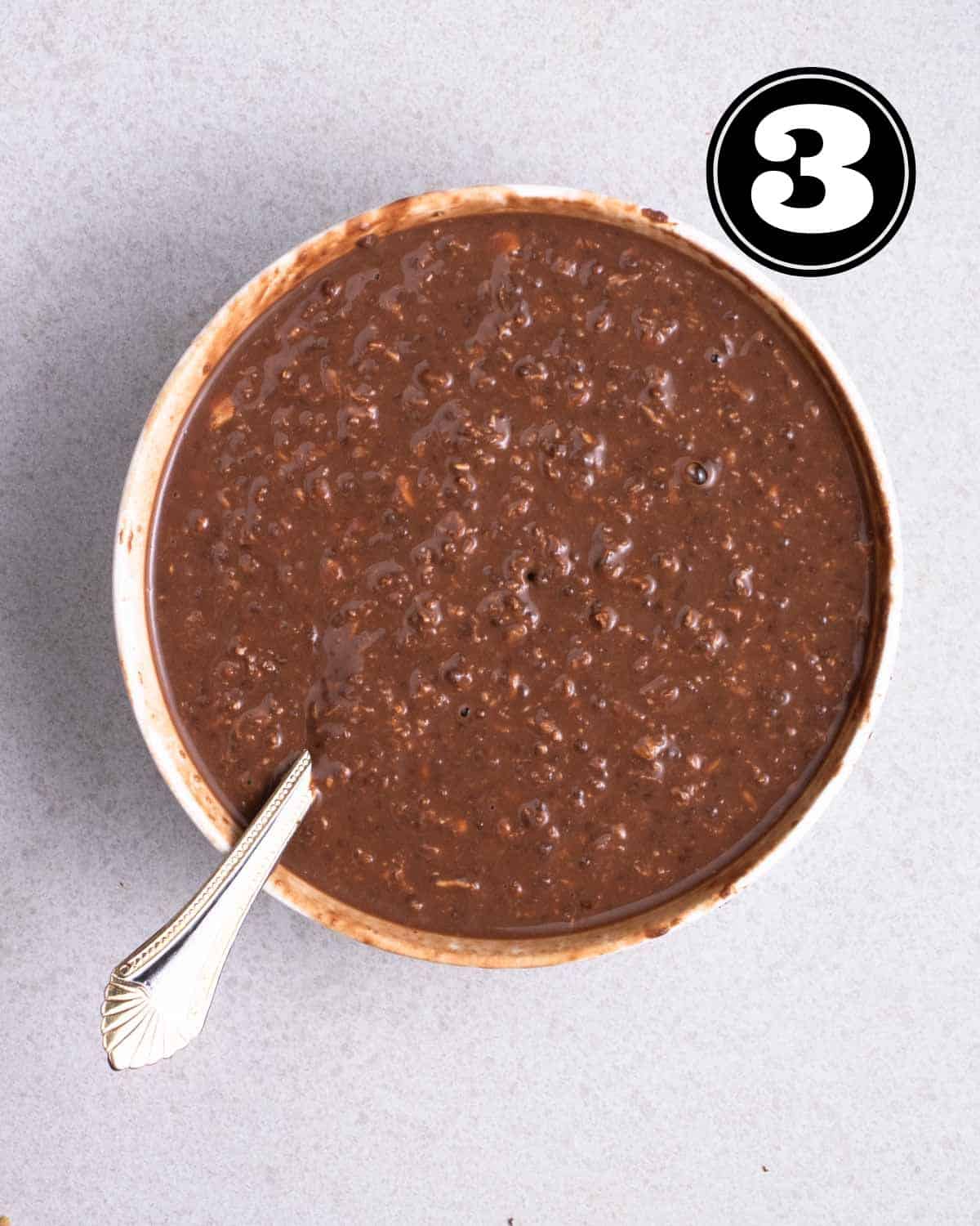 Chocolate overnight oats in a bowl with a spoon beside.