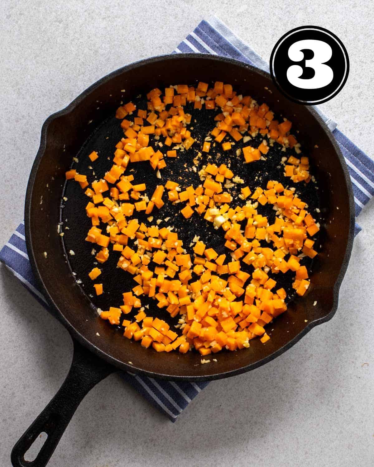 Cooked carrot cubes in a cast iron skillet on a blue striped teacloth.