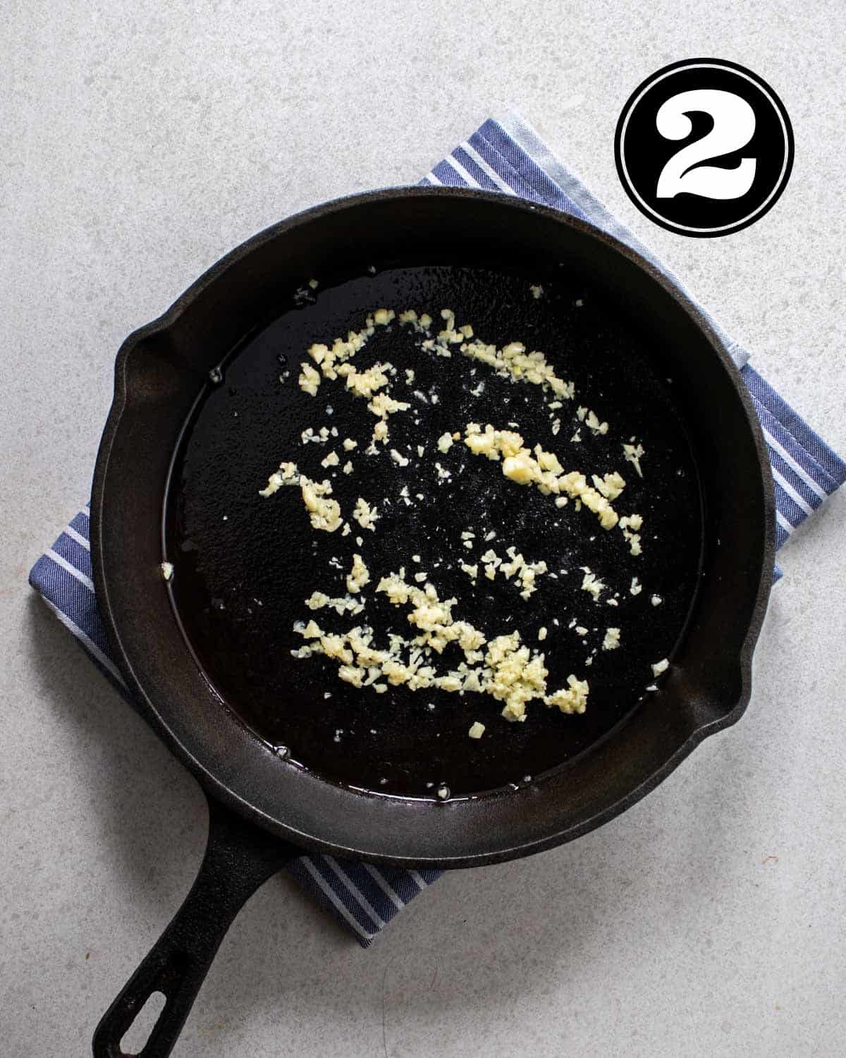 Cooked galric in a cast iron skillet on a folded blue striped teacloth.